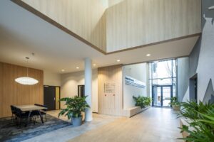 Moderne entreehal van een kantoorgebouw aan de Joop Geesinkweg met houtaccenten, veel daglicht en kamerplanten.